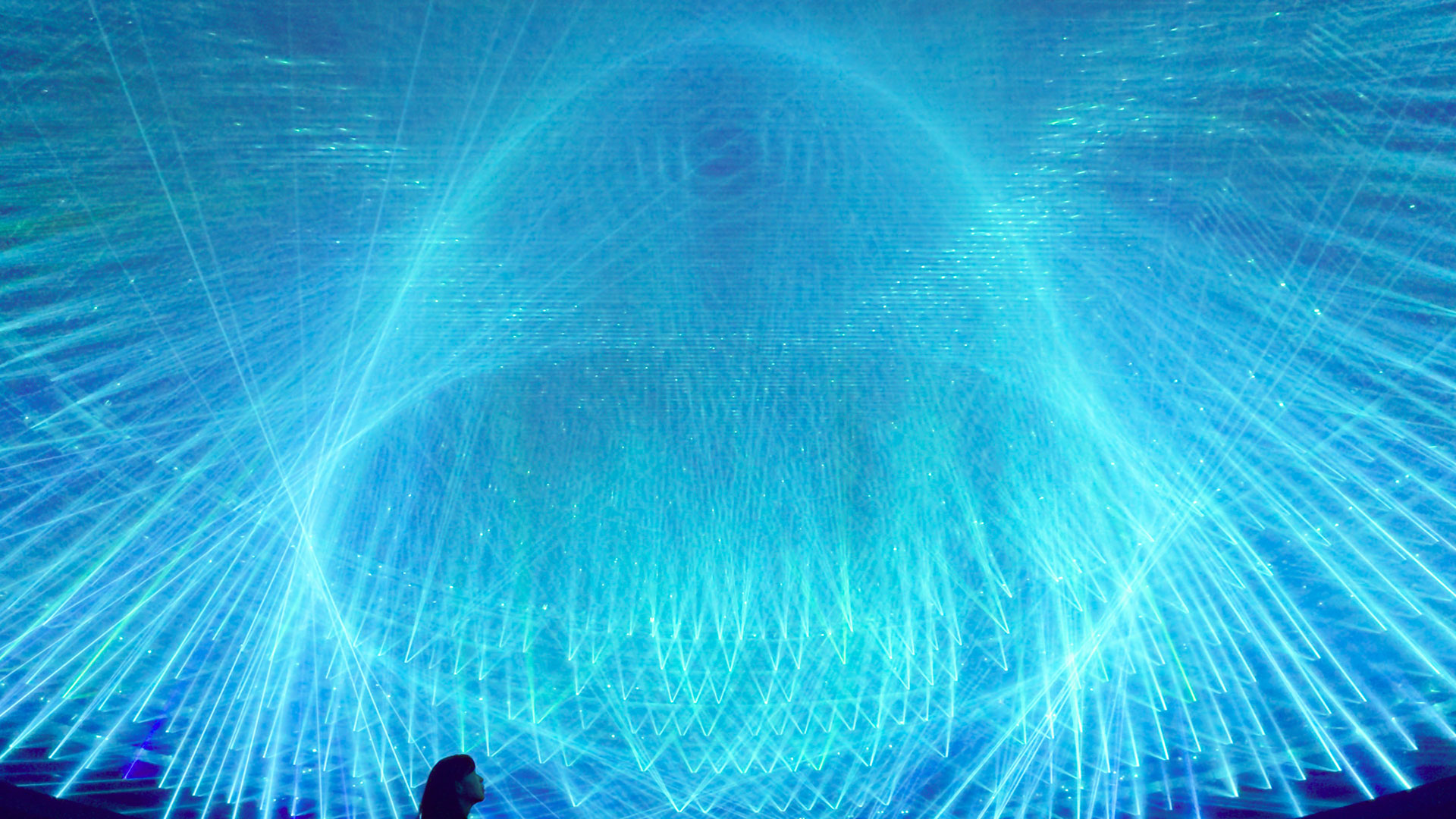 A silhouette of a lady staring up at the blue laser light streaks 