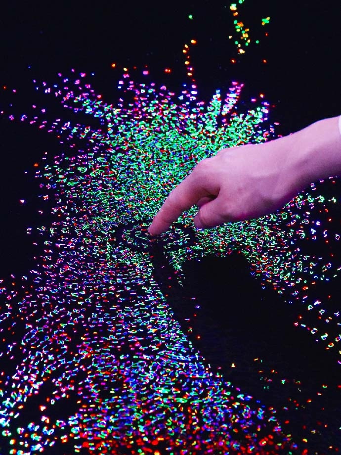 Finger touching the Living Crystallized Light artwork with ripples of water and light