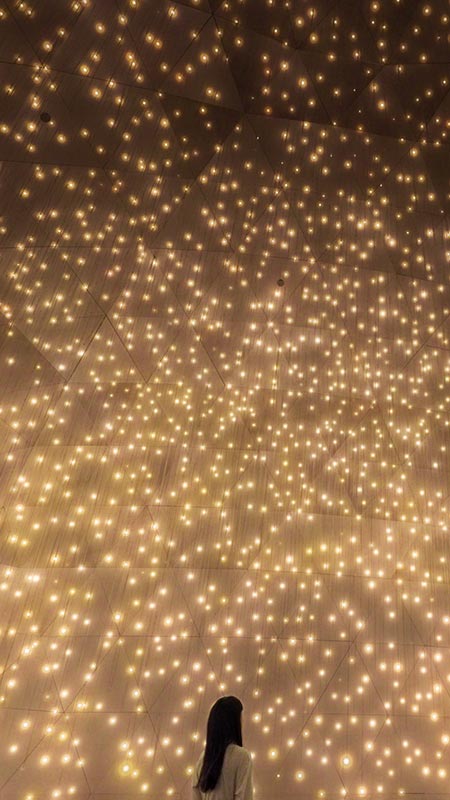 A lady wearing a white dress glazing up looking at bright yellow particles that look like little suns