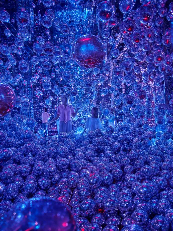 A mother with her son and daughting interacting with floating silver balloons with purple-blue hues in the exhibit.