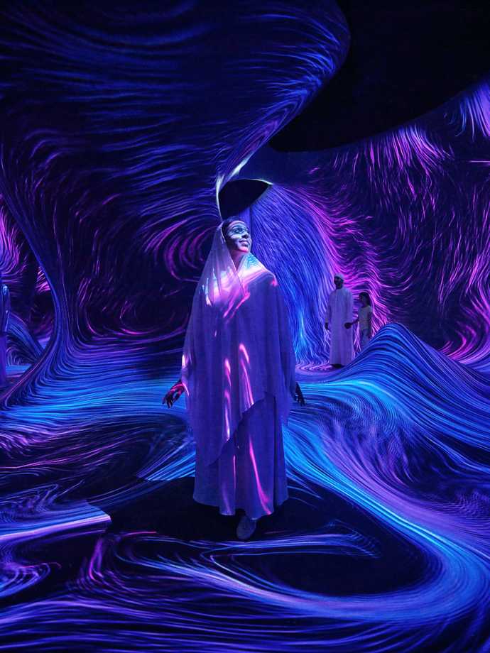 An Emirati woman wearing abaya inside a dark area with purple and blue wavy light streaks all over.