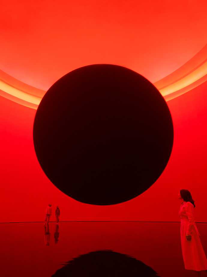 A lady staring at a huge black spot inside a red room.